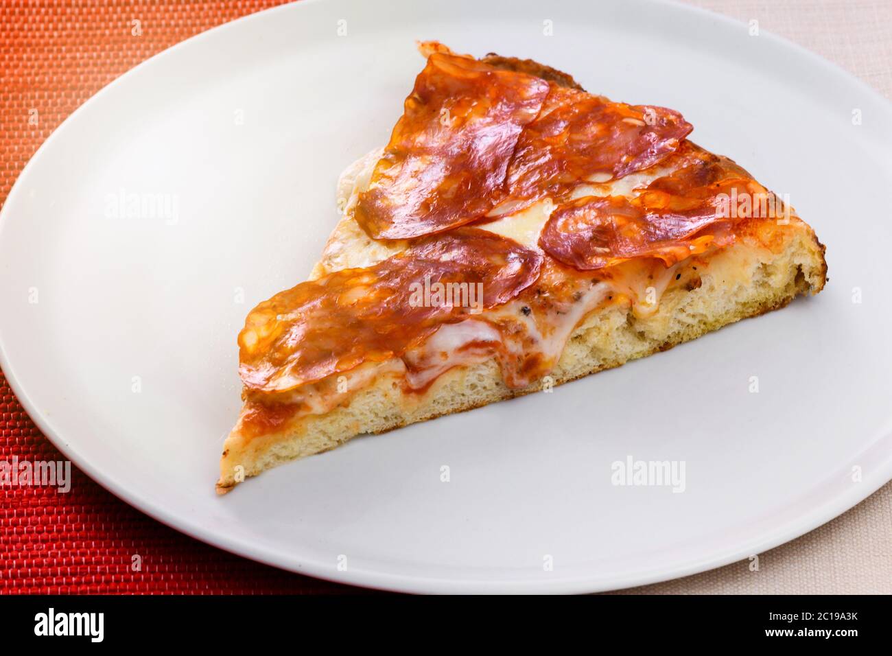 Scheibe traditionelle italienische würzige Salami Pizza Besatz auf einem generischen weißen Teller in der Nähe zeigt die Textur der Basis Stockfoto