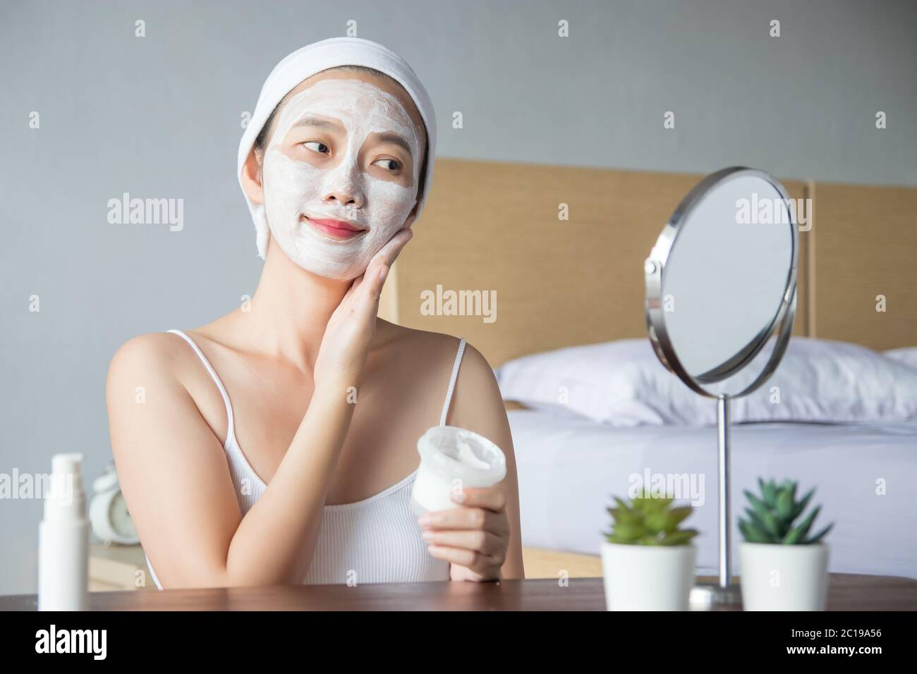 Asiatische Frau Anwendung Feuchtigkeitscreme Gesicht Peeling Peeling weiße Ton Maske auf der Haut, Blick in Spiegel mit Smiley Gesicht mit Creme, Gesicht berühren. Stockfoto