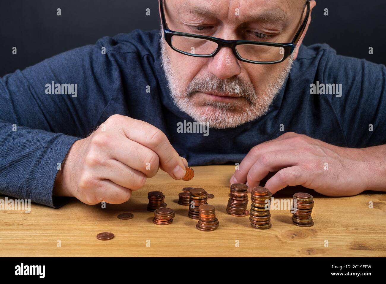 Ein Mann, der in Münzen auf einem Tisch in einer Zeit der Krise zählt Stockfoto