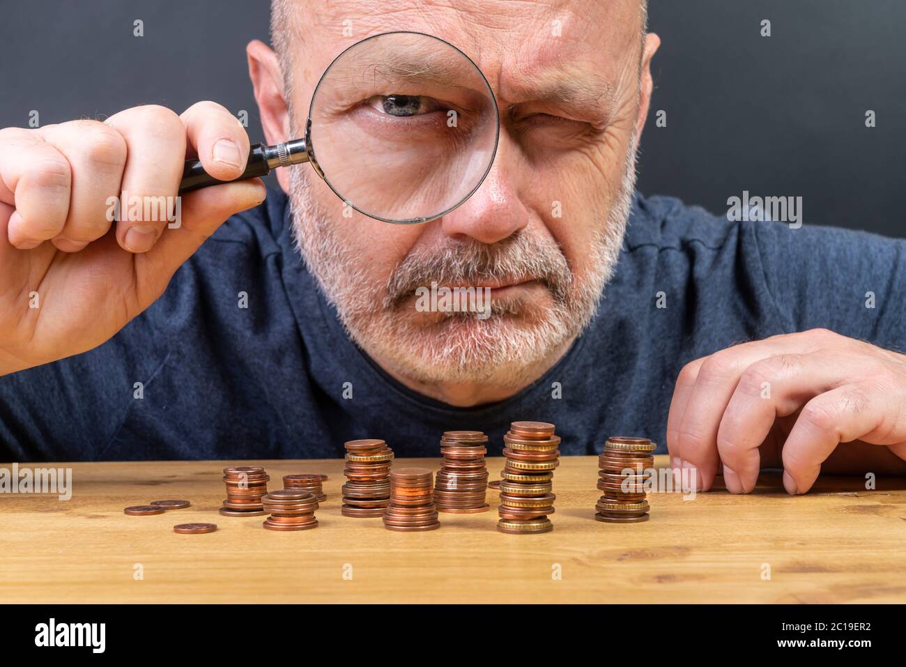 Ein Mann mit einer Lupe, während er in Münzen auf einem Tisch in einer Zeit der Krise zählt Stockfoto