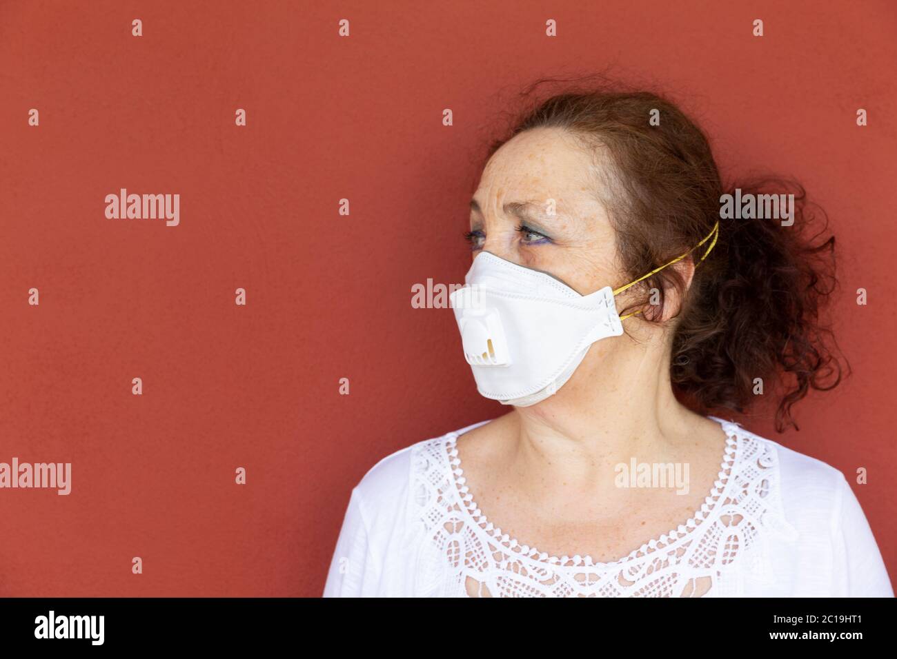 Porträt einer alten Frau mit Schutzmaske auf roter Wand. Einengung durch Coronavirus. Covid-19-Konzept. Stockfoto