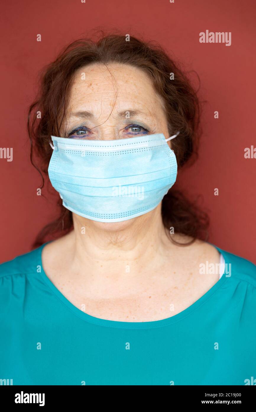 Porträt einer alten Frau mit Schutzmaske auf roter Wand. Einengung durch Coronavirus. Covid-19-Konzept. Stockfoto