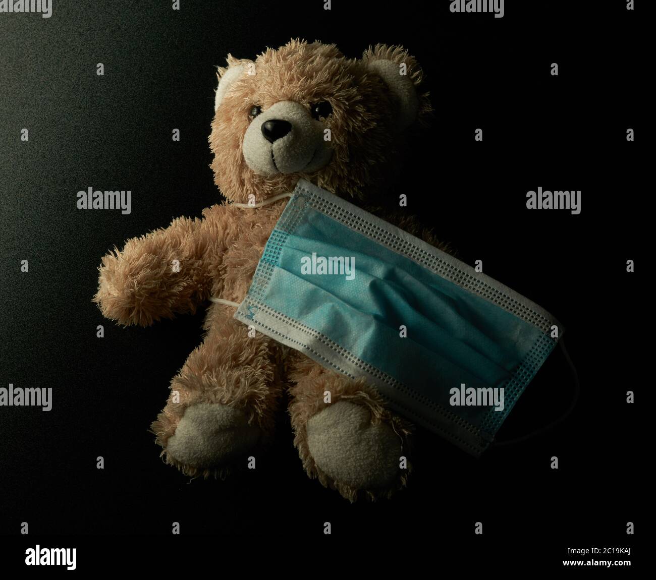 Teddybär mit medizinischer Maske in der Dunkelheit. Kinderschutz verhindert covid-19. Stockfoto