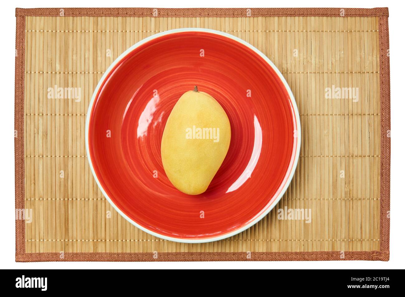 Farbe Stillleben - gelbe Mangofrucht auf einem roten Teller auf einer Rohrservierung Matte Stockfoto