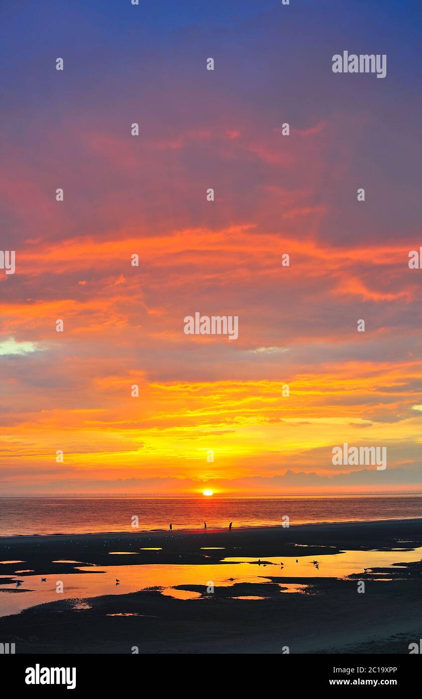 Drei Figuren, die bei Sonnenuntergang am Ufer entlang in Blackpool spazieren Stockfoto