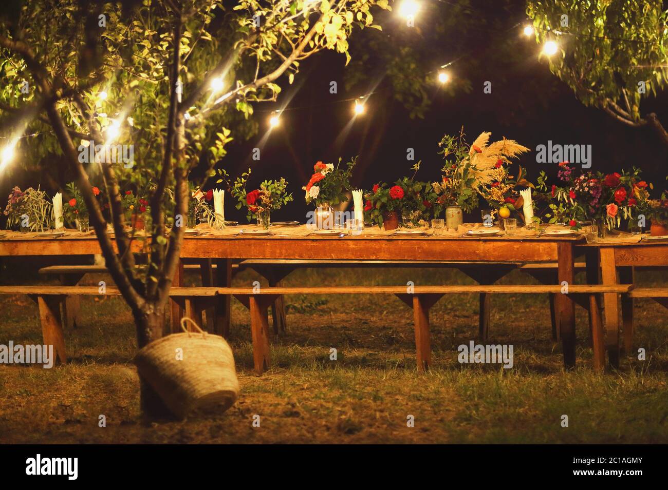 Bereit für ein rustikales Abendessen im Freien bei Nacht mit Weingläser, die Blumen und die Lampen Stockfoto