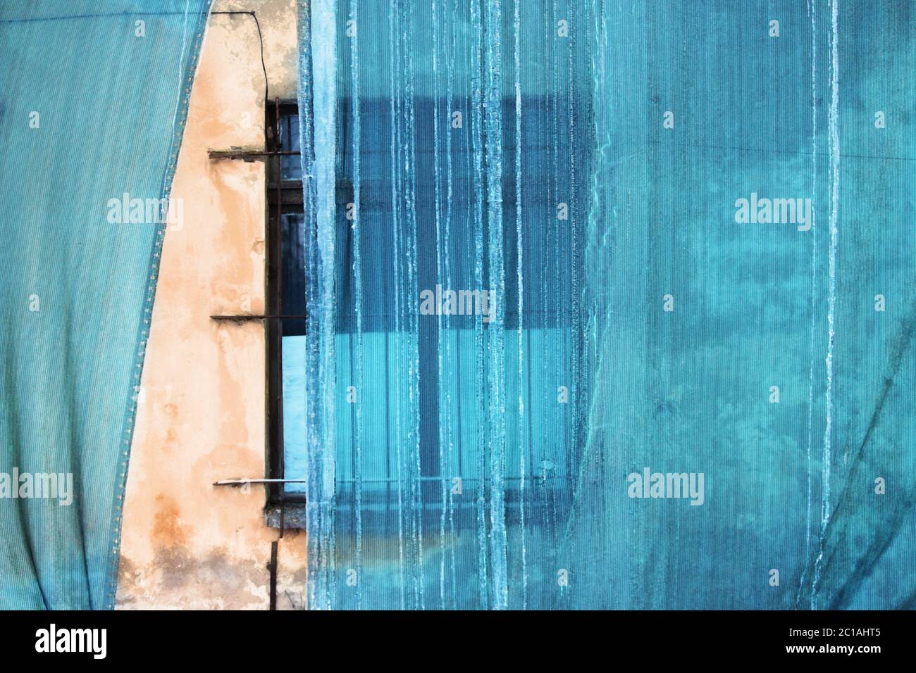 Sanierung des Gebäudes und ein schützendes grünes Gebäudemetz mit gefrorenem Wasser, das vom Dach abfließt. Altes Fenster. Stockfoto