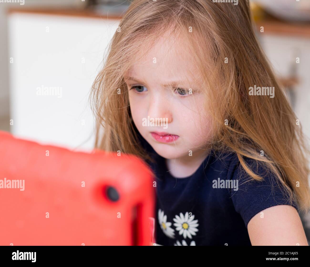 Kleines Mädchen, das etwas auf einem Tablet, Blick aufmerksam auf den Bildschirm, lange dunkelblonde Haare, Pre-School-Kind Blick auf Tablet Stockfoto