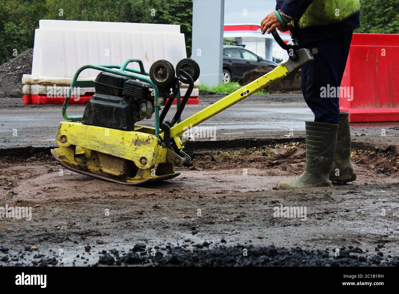 Ein Straßenbauarbeiter verdichtet den Boden mit einer kompakten Vibroplatte, bevor er einen problematischen sumpfigen Abschnitt der Rehe asphaltiert Stockfoto