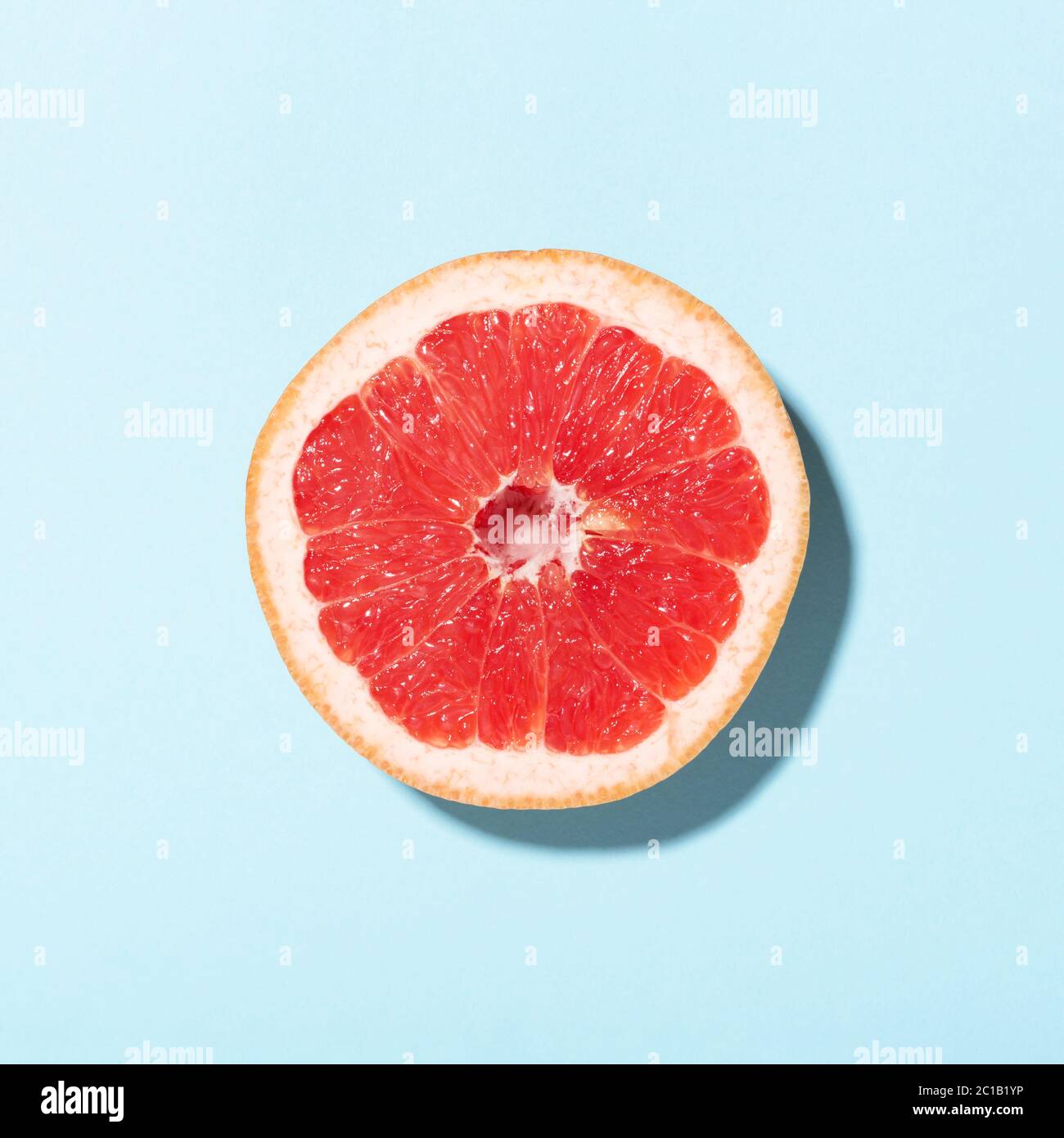 Draufsicht auf Grapefruit-Scheibe im Sonnenlicht auf blauem Hintergrund. Minimalistisches Design. Stockfoto