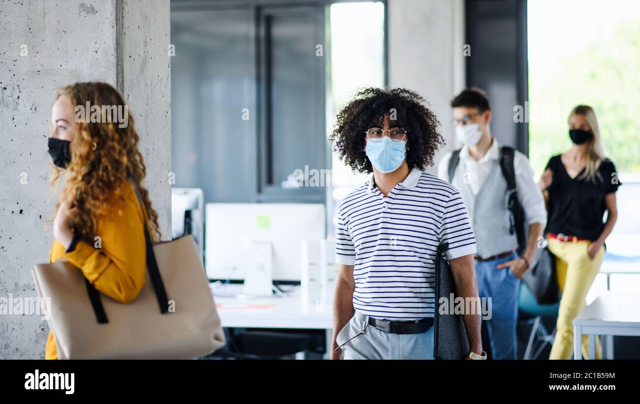 Junge Menschen mit Gesichtsmasken zurück bei der Arbeit im Büro nach Lockdown, zu Fuß. Stockfoto