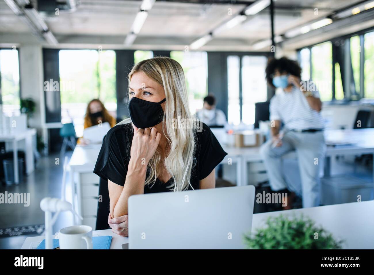 Junge Frau mit Gesichtsmaske wieder bei der Arbeit im Büro nach Lockdown. Stockfoto
