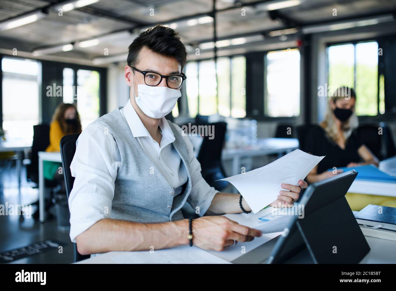 Porträt des jungen Mannes mit Gesichtsmaske zurück bei der Arbeit im Büro nach Lockdown. Stockfoto