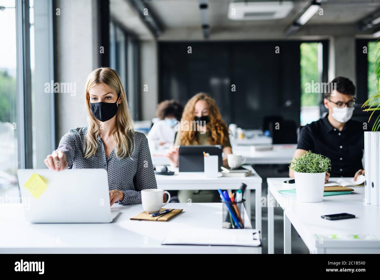 Junge Menschen mit Gesichtsmasken zurück bei der Arbeit oder in der Schule im Büro nach der Sperrung. Stockfoto