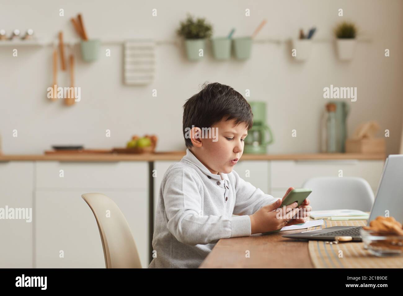 Warm-toned Seitenansicht Porträt von niedlichen Jungen mit Smartphone während des Studiums zu Hause in gemütlichen Innenraum, kopieren Raum Stockfoto