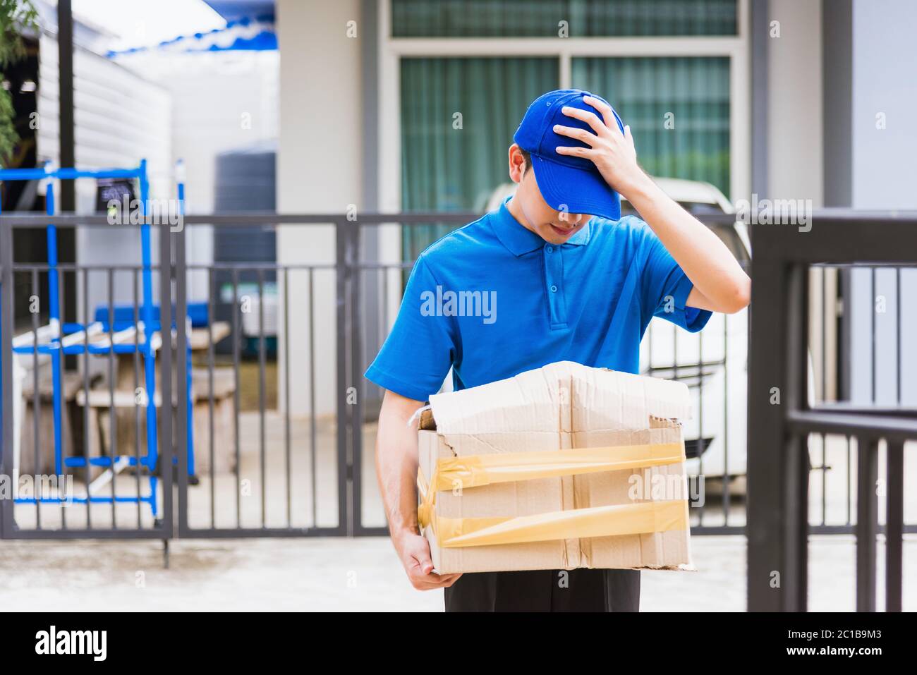 Asiatische junge Lieferung Mann in blauer Uniform er emotional fallen Kurier halten beschädigte Karton ist an der Tür vor Hause gebrochen, Unfall schlechten Transport Stockfoto