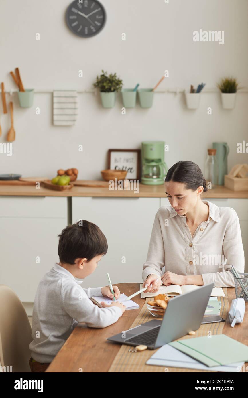 Vertikale warm-getönte Porträt von jungen Mutter und Sohn Hausaufgaben beim Sitzen am Tisch in der gemütlichen Küche, kopieren Raum Stockfoto