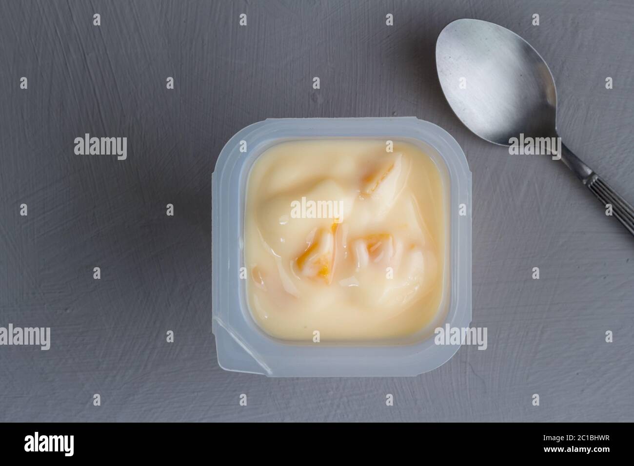 Gesunde Pfirsich Frucht aromatisierten Joghurt mit natürlicher Färbung in Kunststoff-Tasse isoliert auf graue Textur b Stockfoto