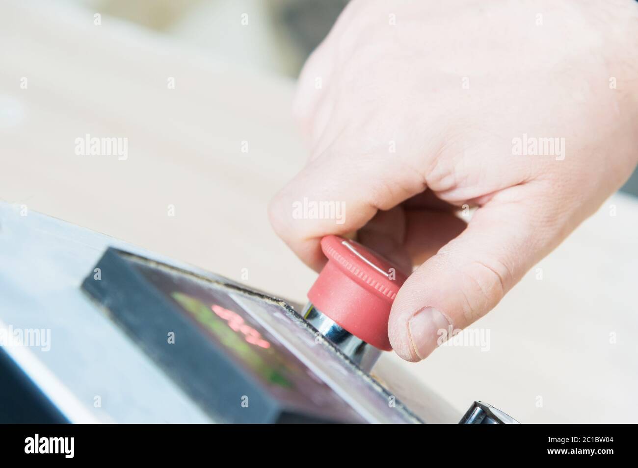 Nahaufnahme der Hand eines Mannes auf einer roten Taste auf dem Bedienfeld. Not-aus oder Start der Anlage und Produktion Stockfoto