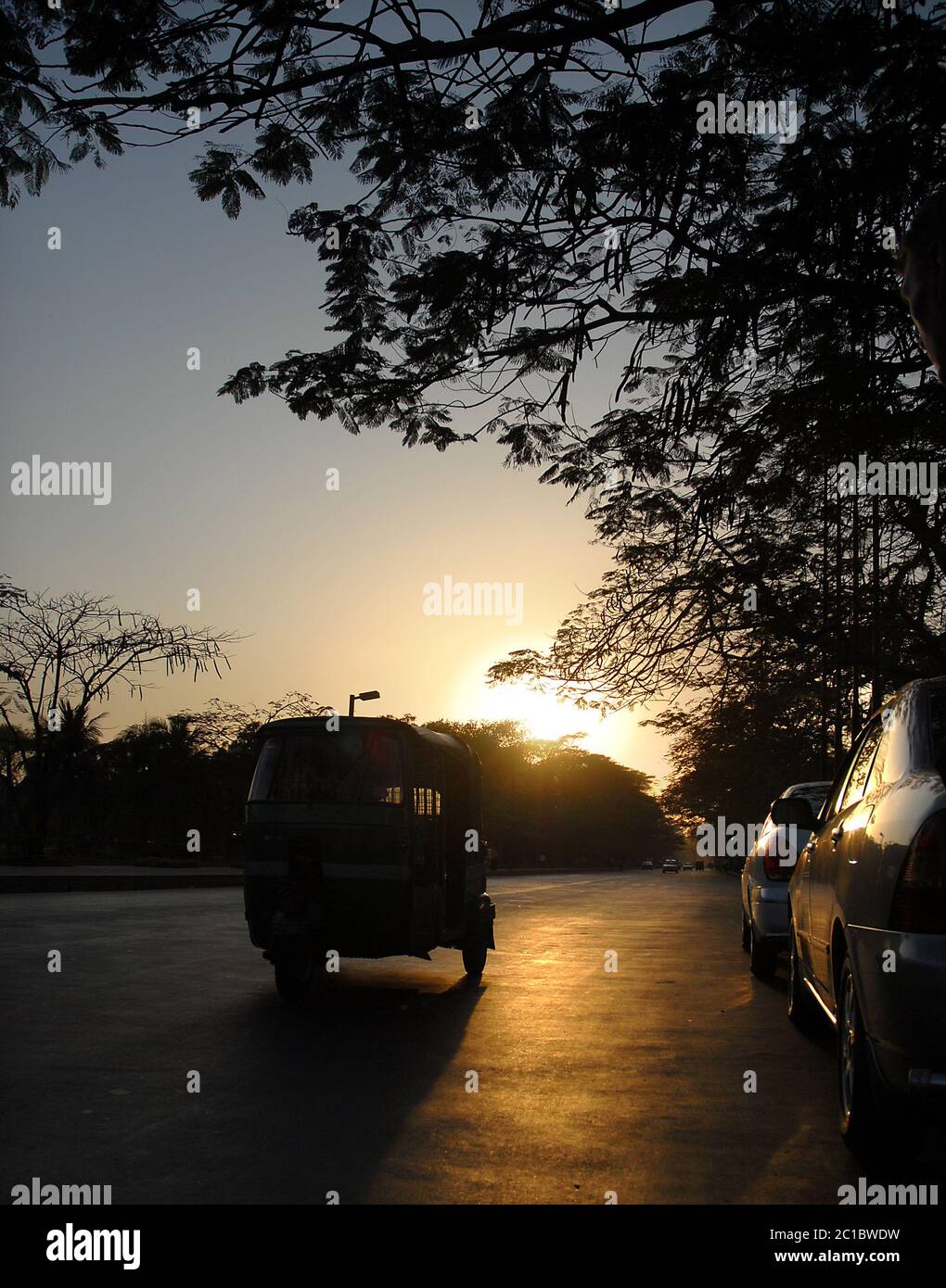 Silhouette einer Auto-Rikscha (Tuk Tuk) auf einer Straße in Dhaka, Bangladesch. Die Rikscha hat die untergehende Sonne hinter sich. Stockfoto