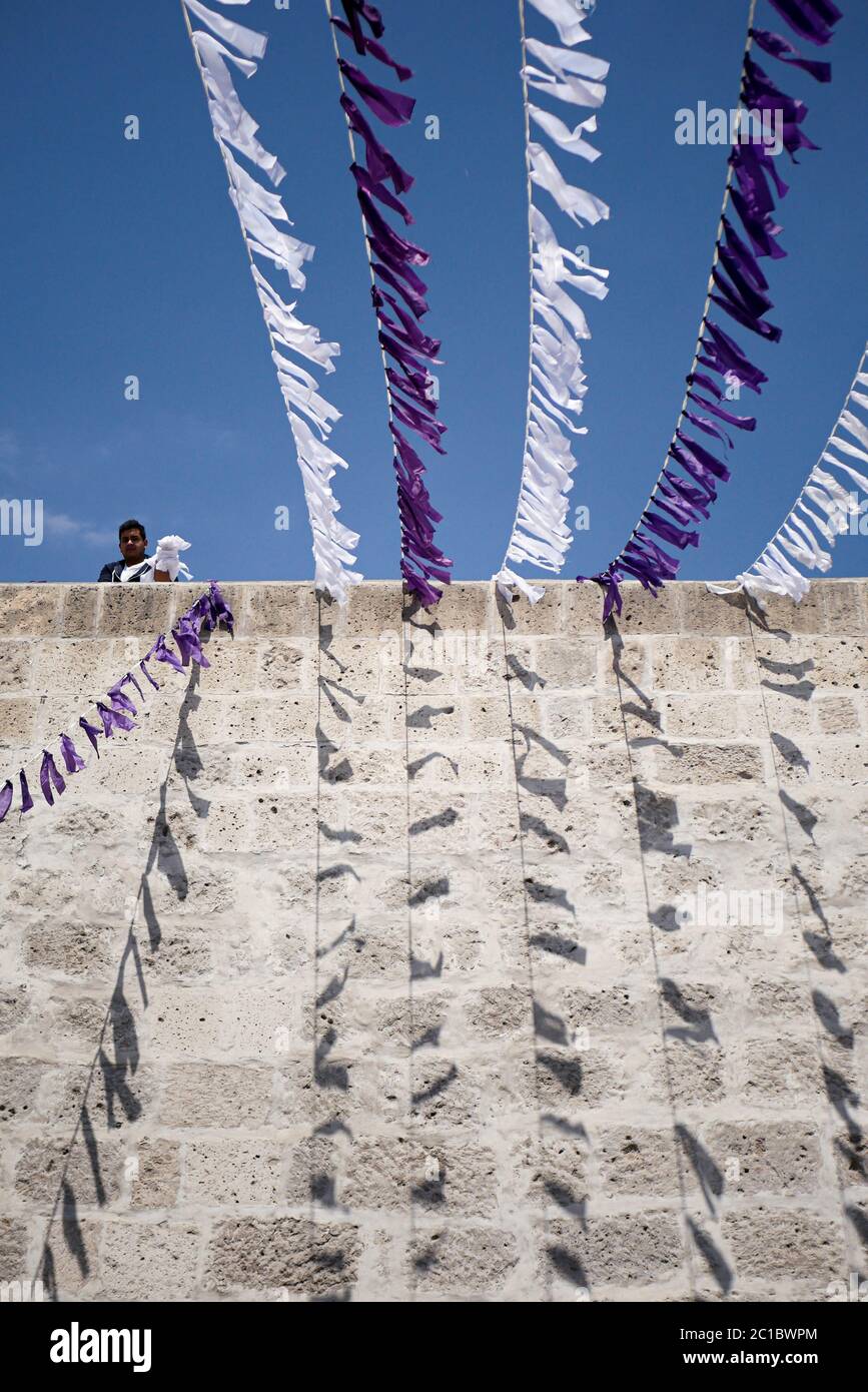 Mann, der die Dekoration für katholische Feiern auf dem Dach des weißen Sillar-Gebäudes im Stadtzentrum von Arequipa, bekannt als die Weiße Stadt, zusammenstellt. Stockfoto