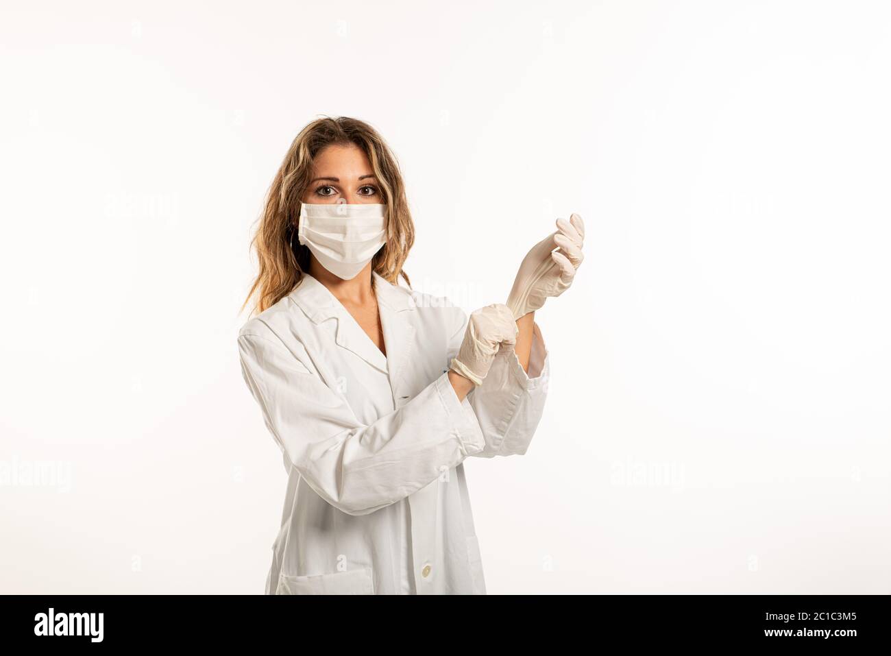 Frau trägt OP-Maske, medizinische Uniform und Schutzhandschuhe auf weißem Hintergrund Stockfoto