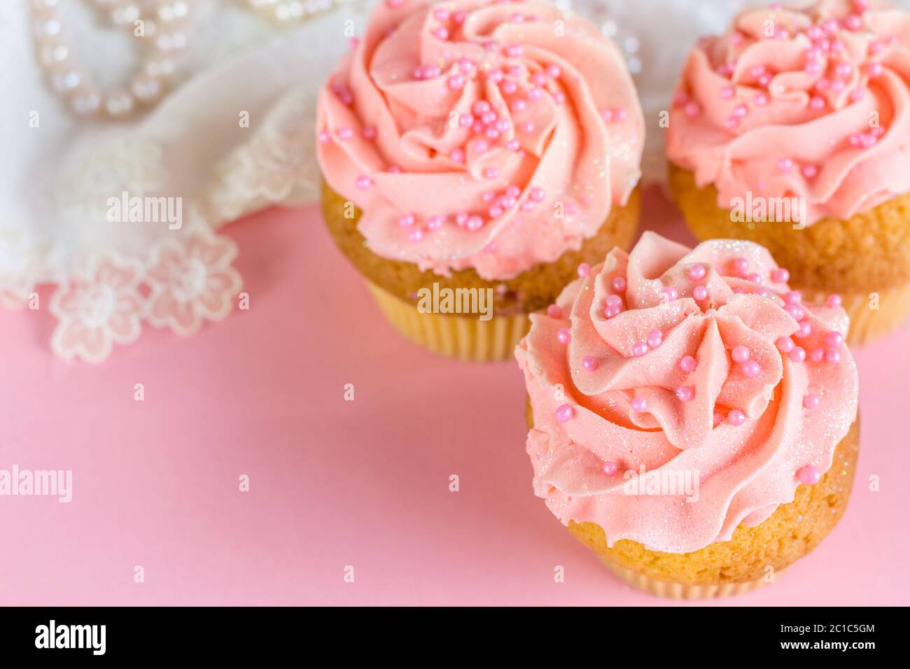 Rosa Glitzer und Perle verziert Tasse Kuchen aus nächster Nähe auf rosa Hintergrund mit defokussierten Spitze und Perle Stockfoto