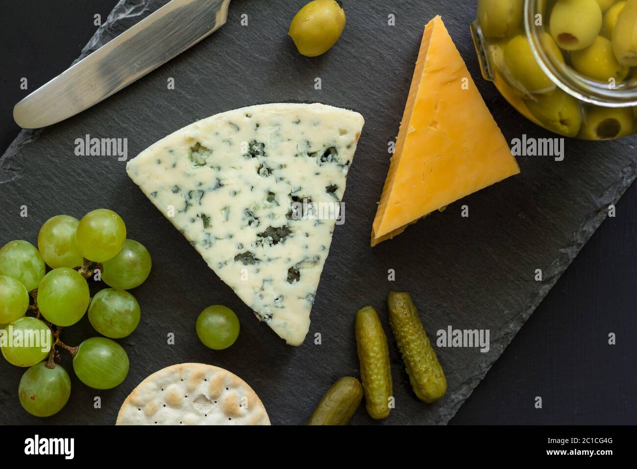 Käseplatte mit Blauschimmelkäse, gelbem Cheddar, Oliven, Trauben und Cracker Stockfoto