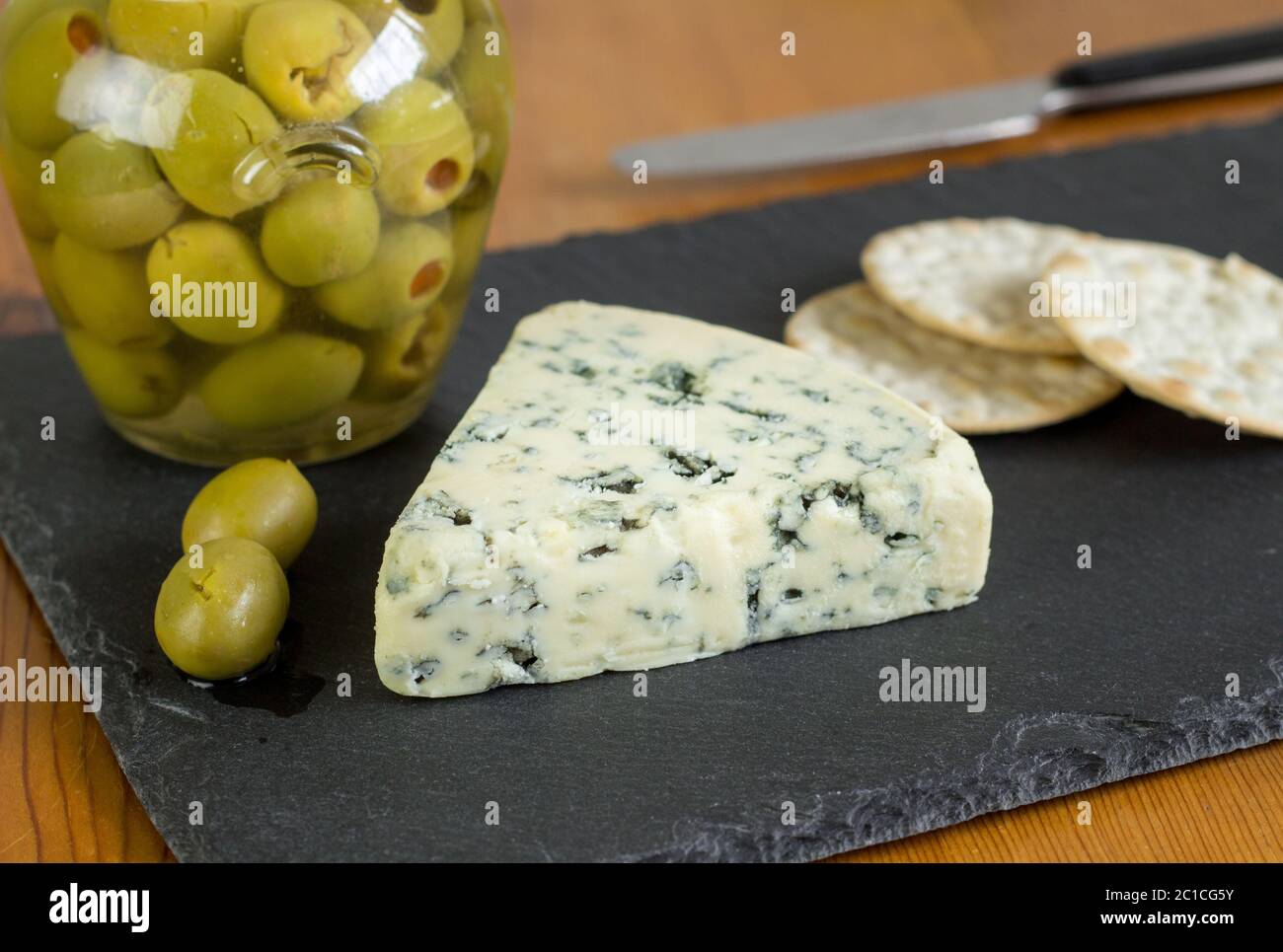 Blauägekäse auf Schiefer mit Glas gefüllte Oliven - Stilton oder Roquefort Typ Käse close up o Stockfoto