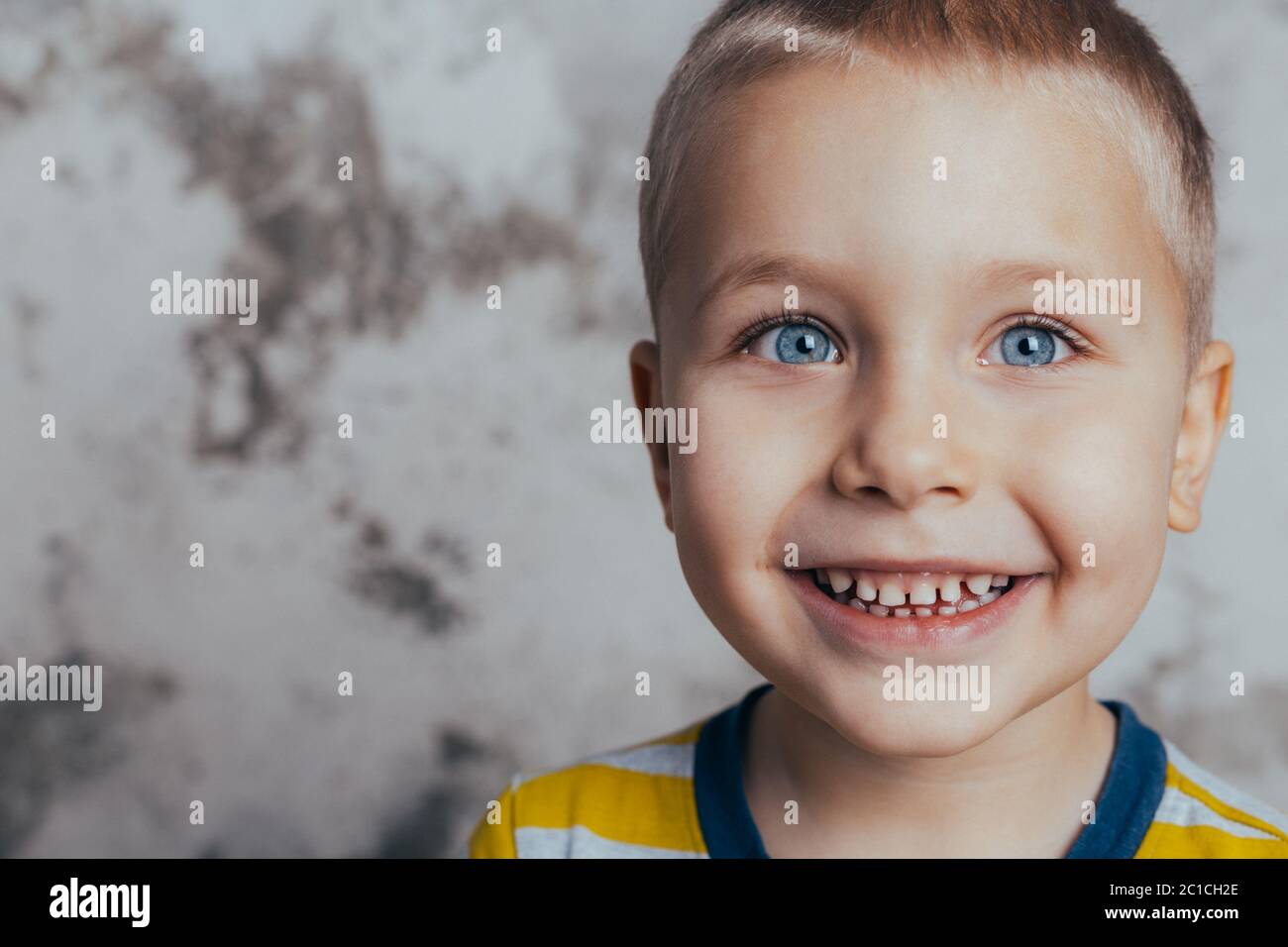 Kleiner Junge posiert vor einer grauen Betonwand. Porträt eines lächelnden Kindes in einem gelb gestreiften T-Shirt Stockfoto