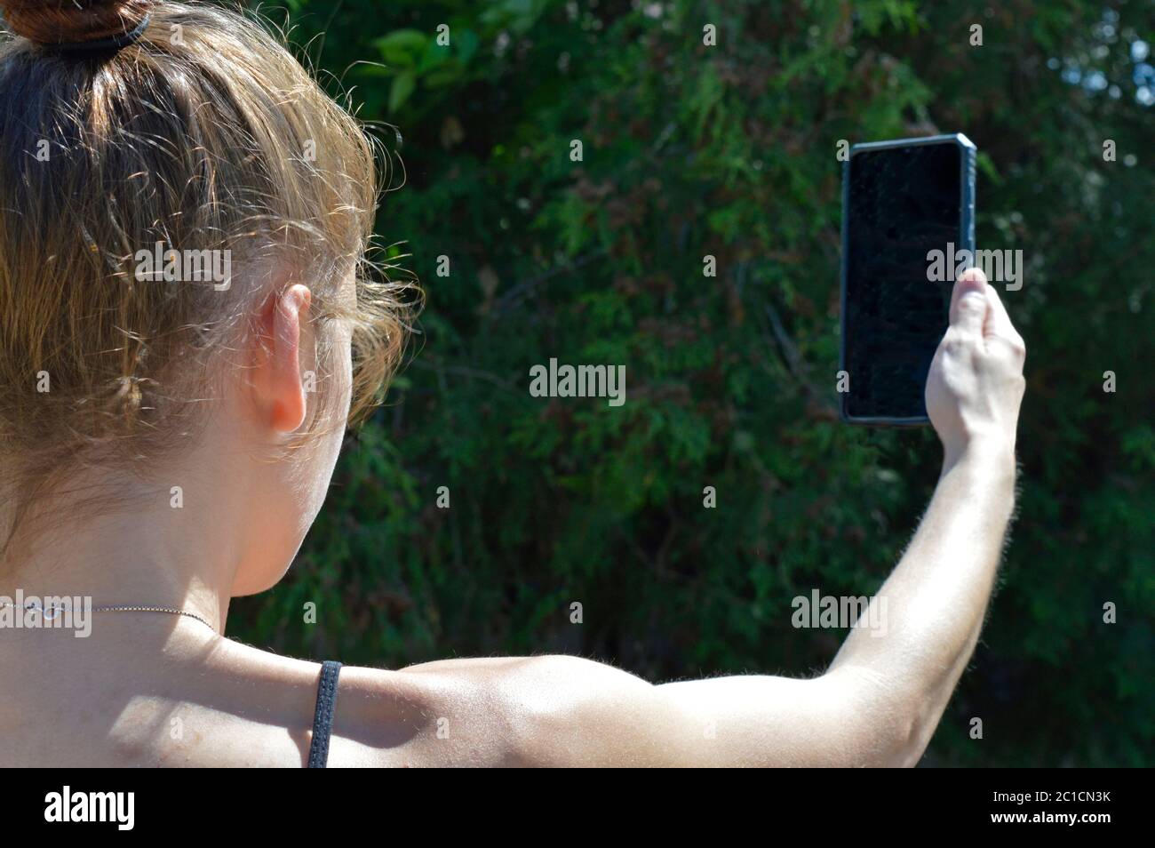 Mädchen im Wald auf der Suche nach Handy-Signal oder möglicherweise mit einem G5-Signal. Der Bildschirm des Smartphones ist schwarz, sodass Designer Nachrichten oder Symbole einfügen können. Stockfoto