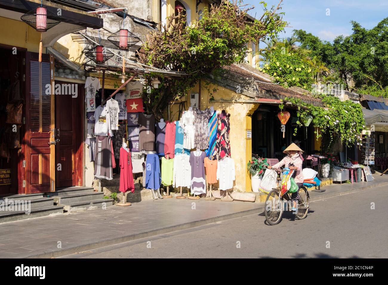 Bekleidungsgeschäft mit einheimischen Frau, die an der Straße in der Altstadt vorbeiradelt. Hoi An, Provinz Quang Nam, Vietnam, Asien Stockfoto