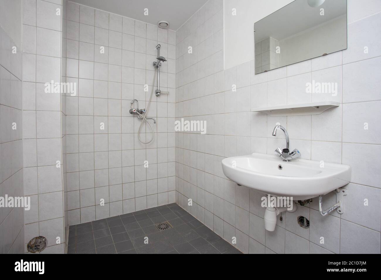 Einfaches, altes, sauberes Badezimmer mit weiß gefliestem Waschbecken und Dusche Stockfoto