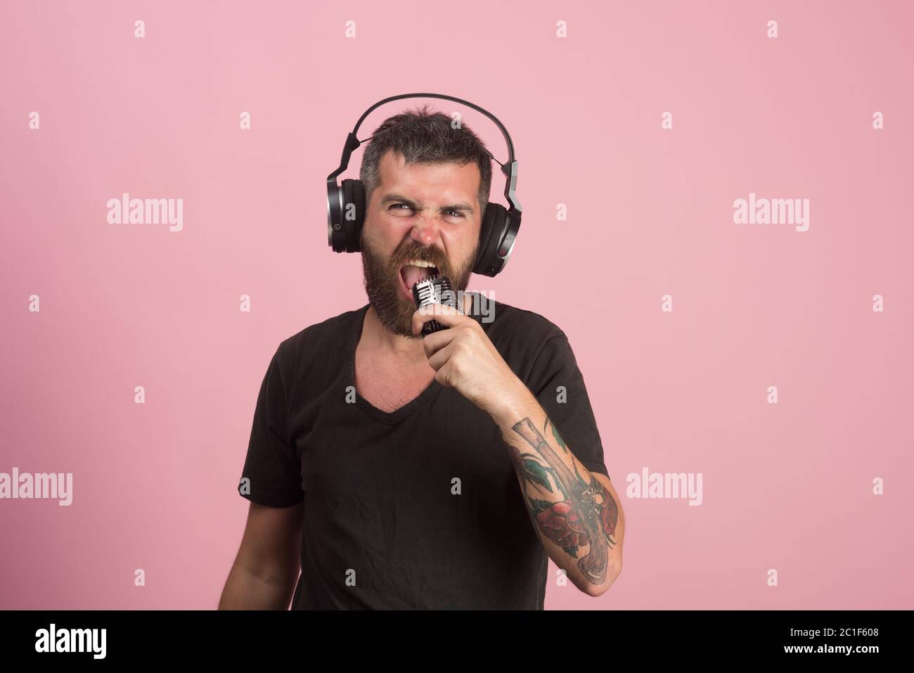 Entspannung und Musikkonzept. DJ mit Bart trägt Kopfhörer. Mann singt ins Mikrofon auf rosa