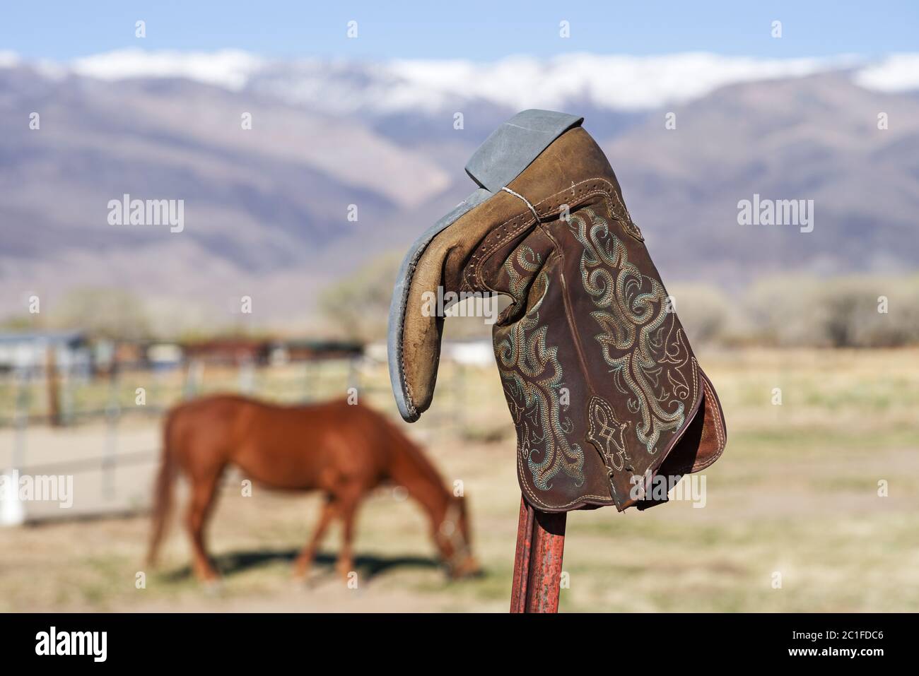 Alter Cowboy Boot auf Fencepost mit unfokussigem Pferd und Berg im Hintergrund Stockfoto