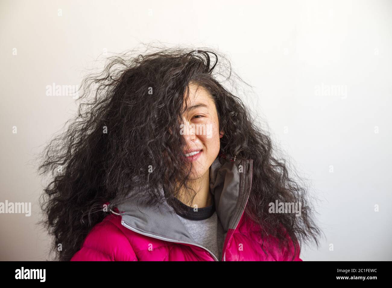 asiatische Frau mit verrückten großen welligen Haar bedeckt die Hälfte ihres Gesichts Stockfoto