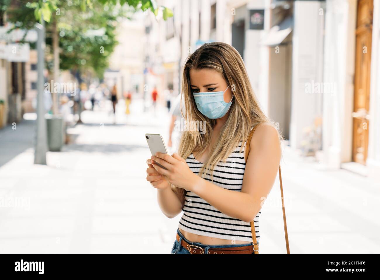 Frau in Maske in der Stadt mit ihrem Handy während der Coronavirus-Pandemie Stockfoto