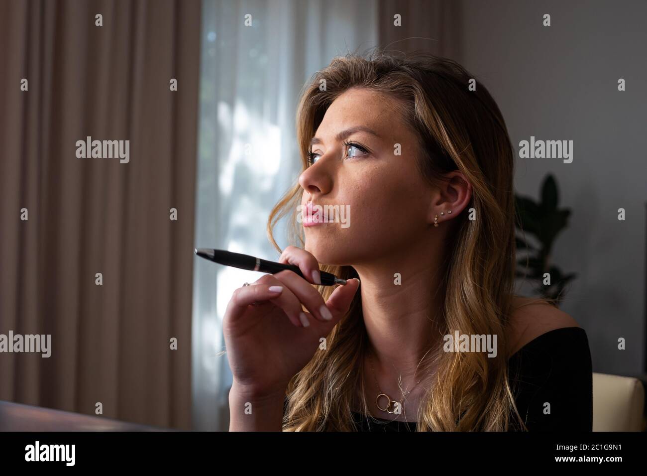 Profil einer jungen Frau mit Stift und Denken zu Hause. Arbeiten von zu Hause aus. Nahaufnahme. Stockfoto