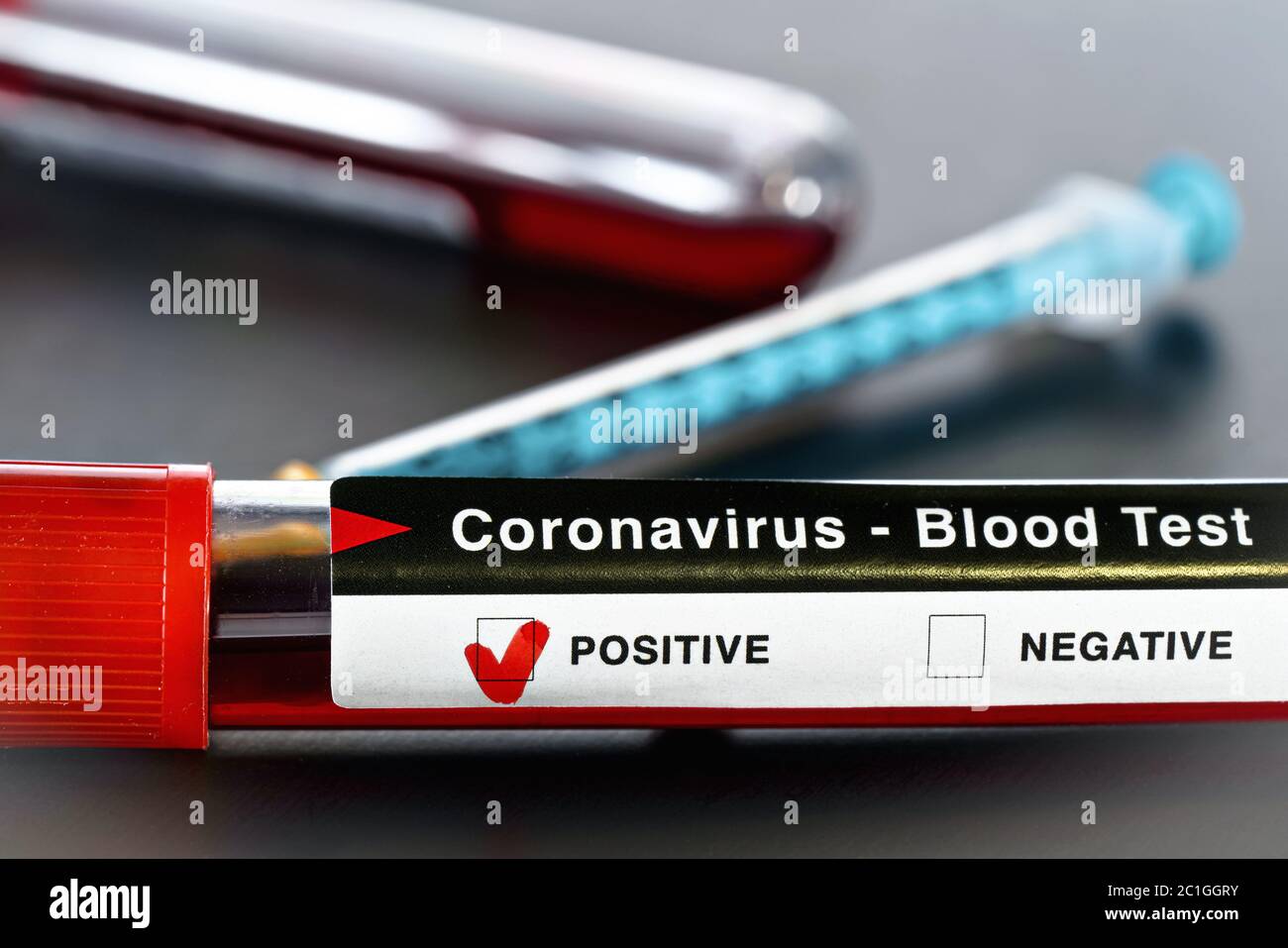 Probe medizinische Fläschchen mit Blut, Etikett sagt Coronavirus-Test, positives Ergebnis. Spritze in der Nähe verschwommen. Covid-19-Tests während des Ausbruchskonzepts Stockfoto