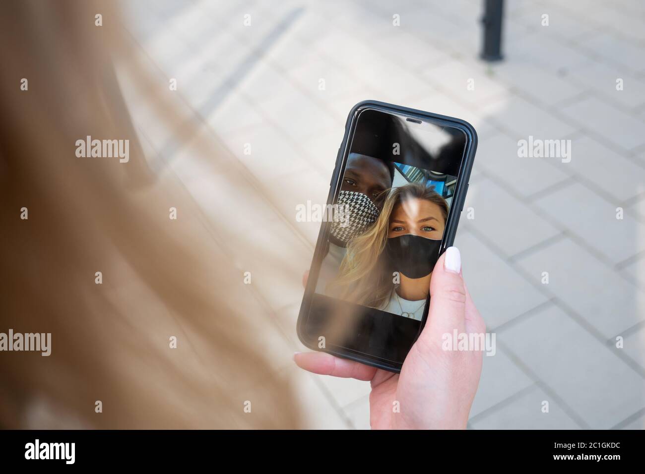 Gemischtes Rennen Paar Gesichtsmaske Selfie auf Telefonbildschirm. Über die Schulter. Im Freien. Stockfoto
