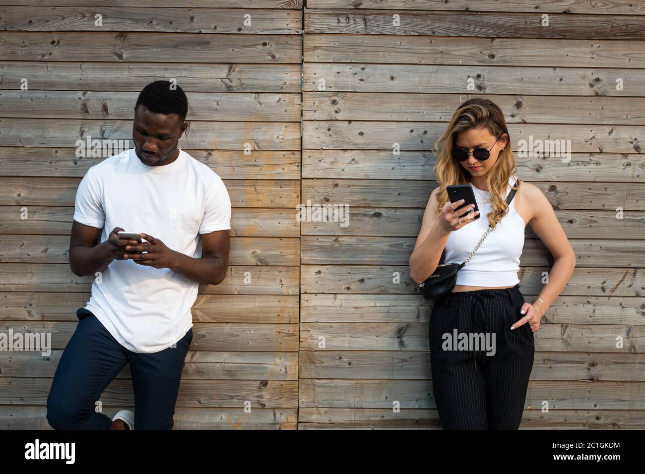 Junger schwarzer Mann und blonde kaukasische Frau mit coolen Einstellungen Blick auf Telefonbildschirme im Freien. Mittlere Aufnahme. Stockfoto