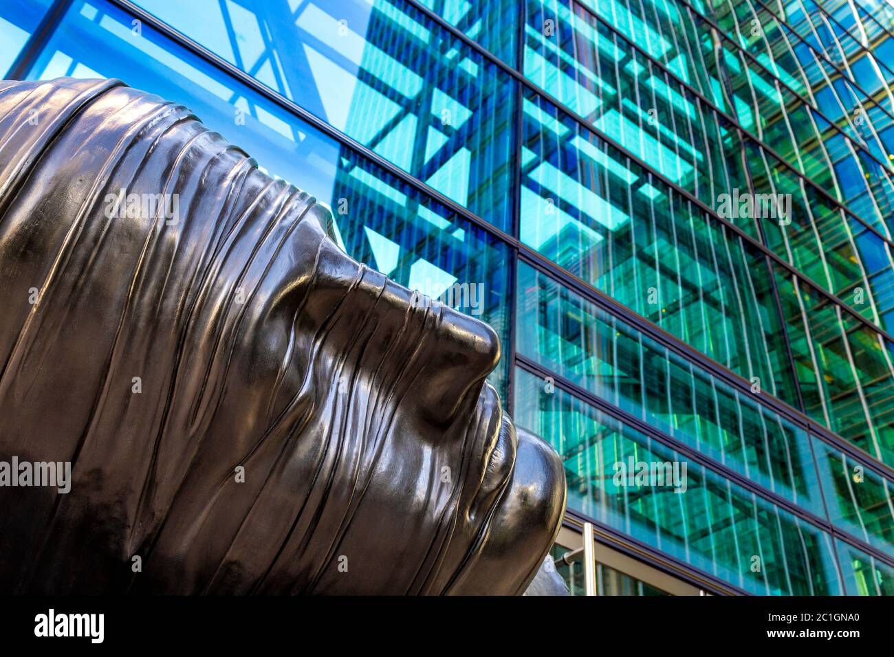 Nahaufnahme der Skulptur eines Kopfes von Igor Mitoraj 'Testa Addormentata' (1983) gegen das zeitgenössische Glasgebäude, Canary Wharf, London, Großbritannien Stockfoto
