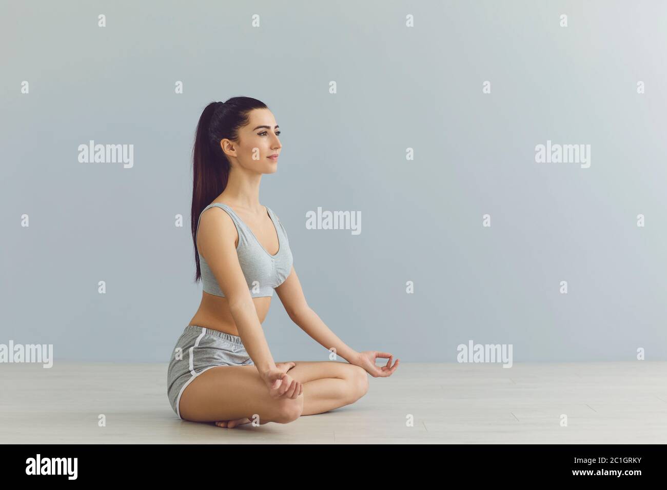 Seitenansicht der Brünette in Lotusposition. Frau in Yoga-Meditation, grauer Hintergrund, Kopierraum. Stockfoto