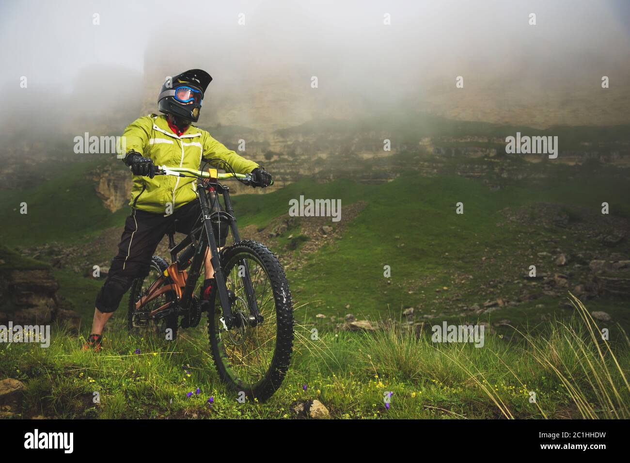 Ein erwachsener mtb-Radfahrer auf einem Mountainbike am Fuße einer Klippe, umgeben von grünem Gras. Niedrige Wolken. Nordkaukasus. Russland Stockfoto