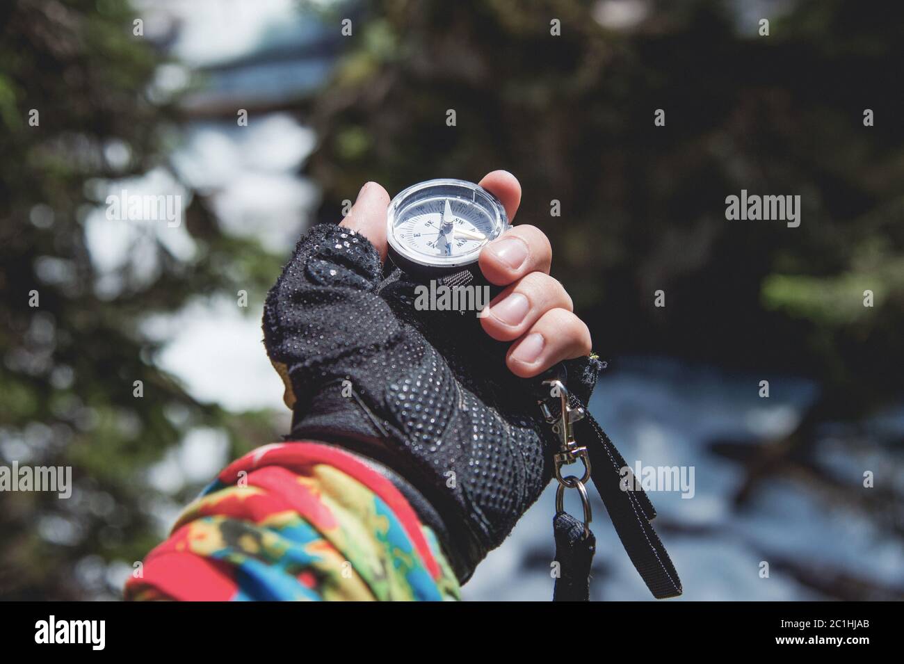 Eine Handschaufel hält einen magnetischen Kompass vor dem Hintergrund eines Nadelwaldes und eines Bergflusses. Das Konzept des Outdoor Stockfoto