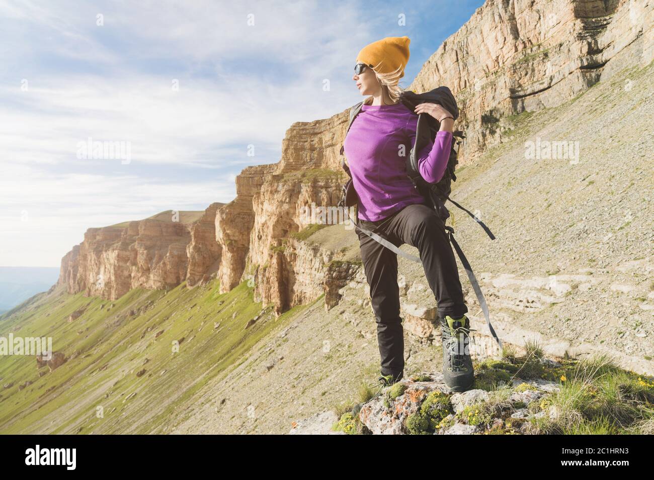 Mädchen Tourist in Sonnenbrille setzt einen Rucksack auf die Natur auf einem Hintergrund von epischen Felsen Vorbereitung für Trekking mit Klettern Stockfoto