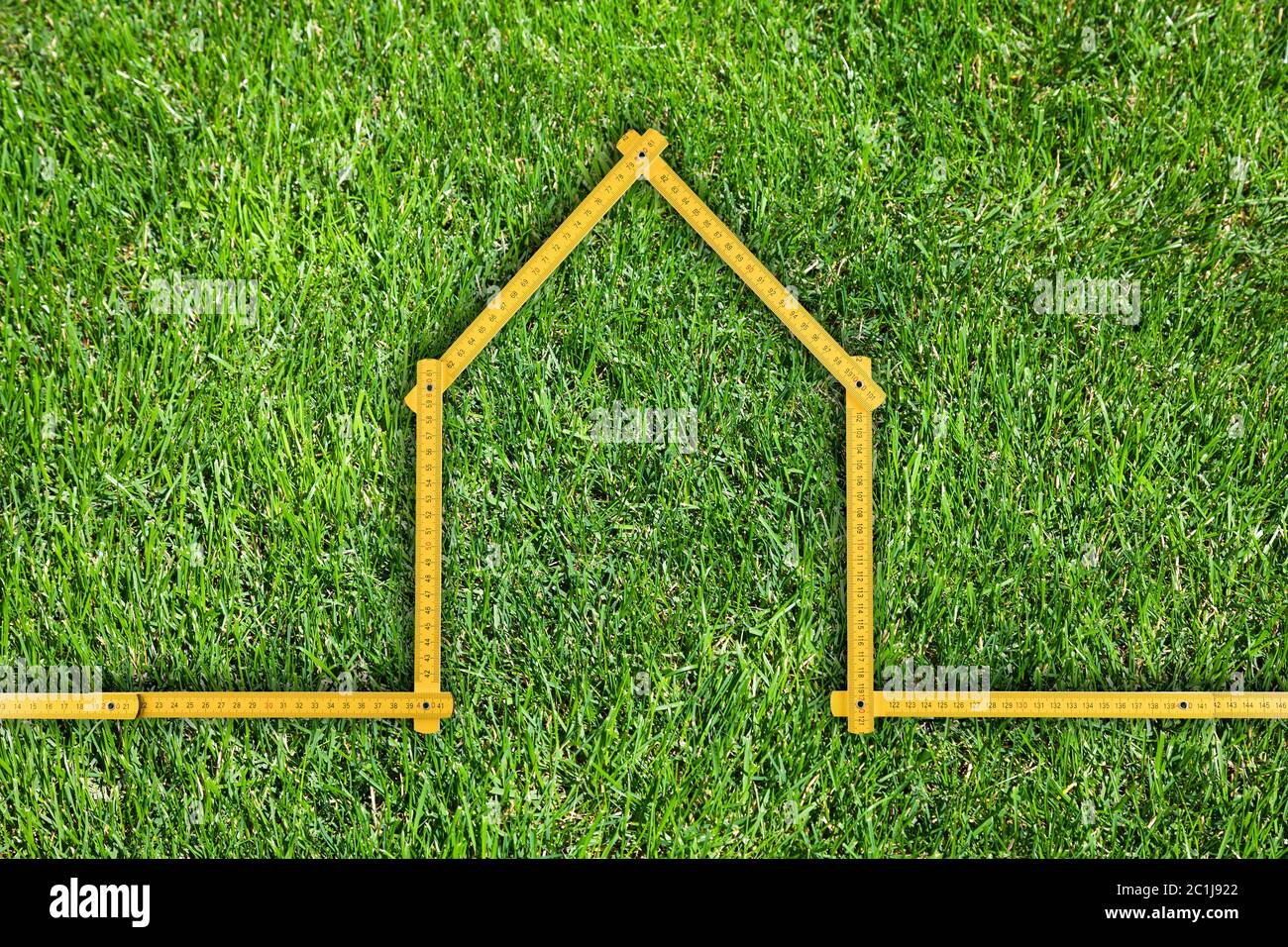 Gelb m Herrscher gefaltet als Haus auf grünem Gras isoliert Stockfoto