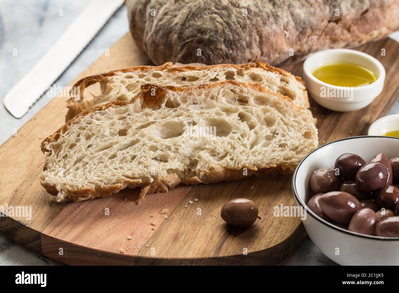 Brotscheiben auf Holzbrett - selektiver Fokus auf italienischen Ciabatta mit Oliven Stockfoto