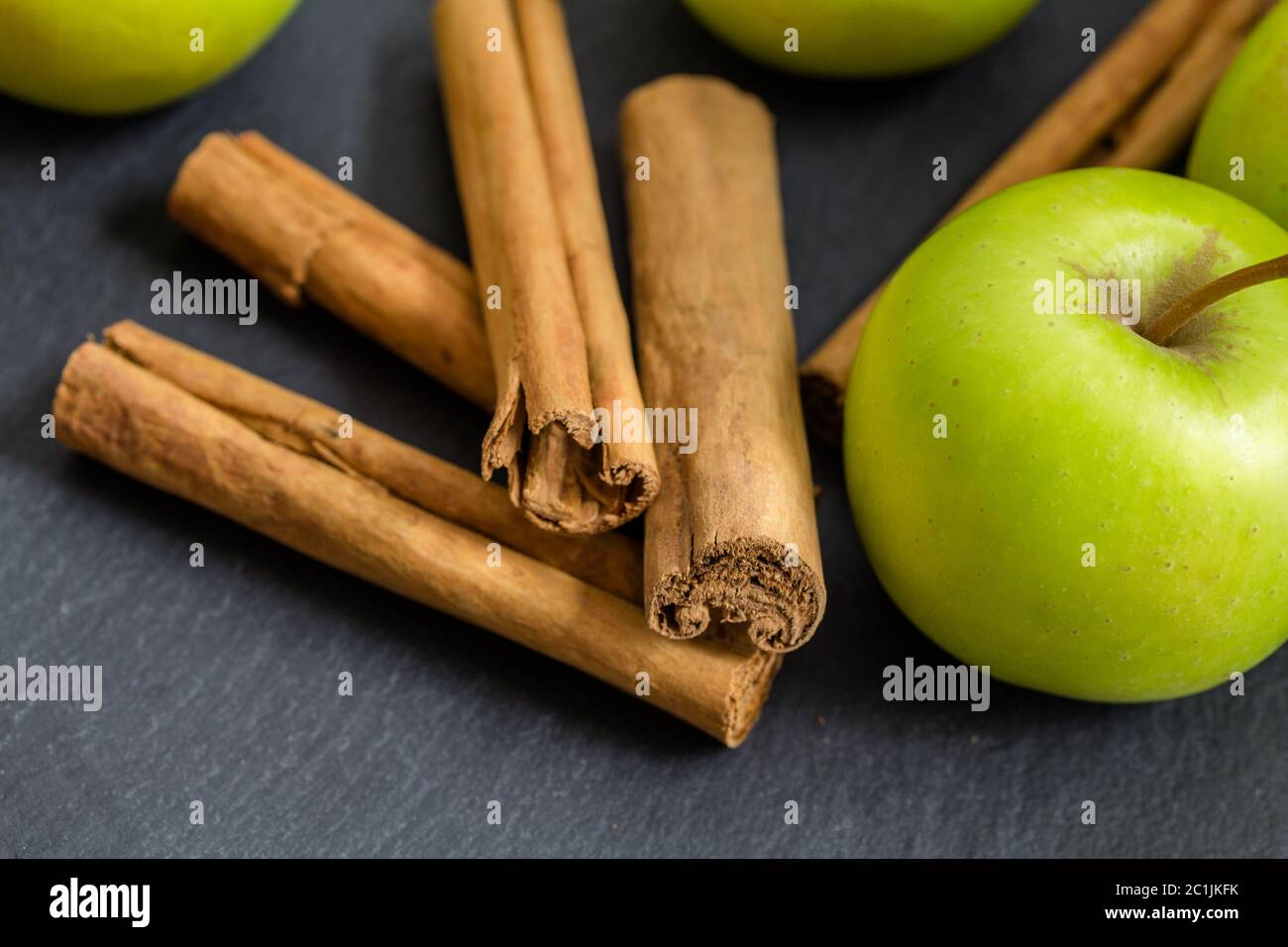 Zimtstangen schließen bis auf schwarzer Schiefer mit grünem Apfel selektiven Fokus - Gewürz Hintergrund Stockfoto