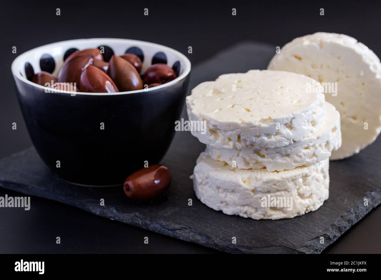 Feta Käse auf schwarzem Schiefer Hintergrund mit Oliven - selektive Fokus auf Käse Stockfoto
